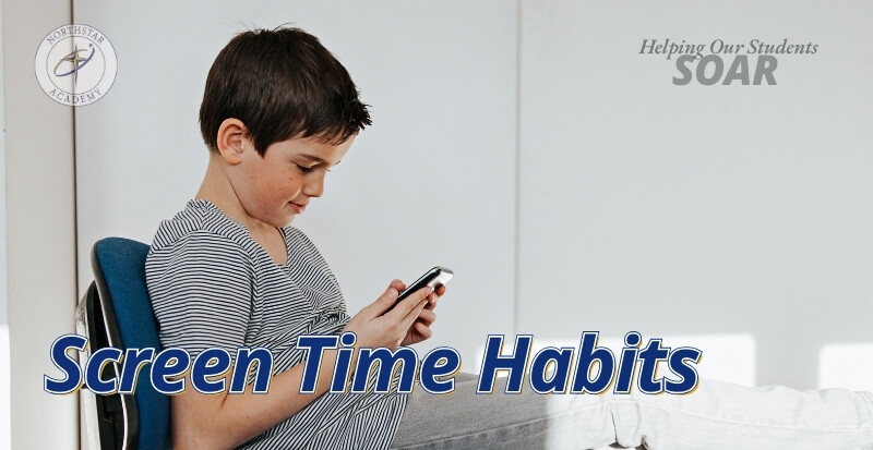 A boy looks at his cell phone while sitting on a chair with his legs up